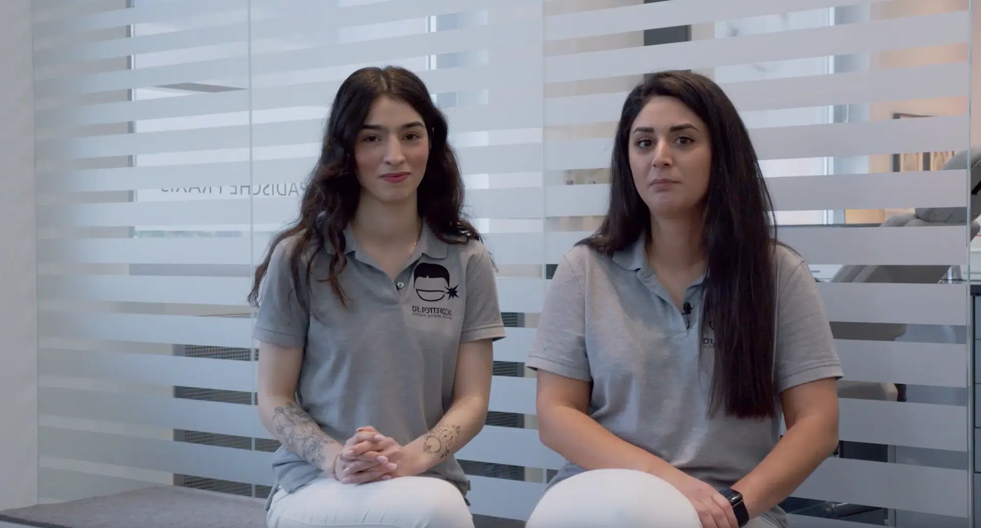 Zwei Frauen in grauen Poloshirts sitzen in einer Kieferortopädischen Praxis. Recruiting Situation.