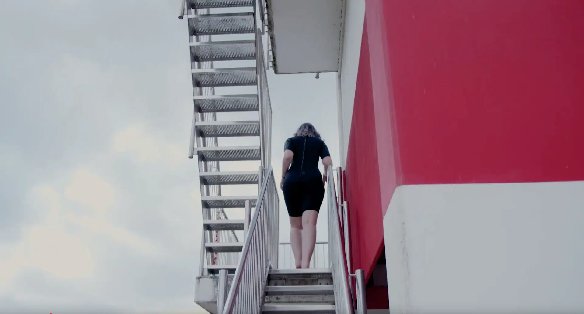 Person geht Treppe hoch, rote Gebäudewand, Schwinnband Sprungturm